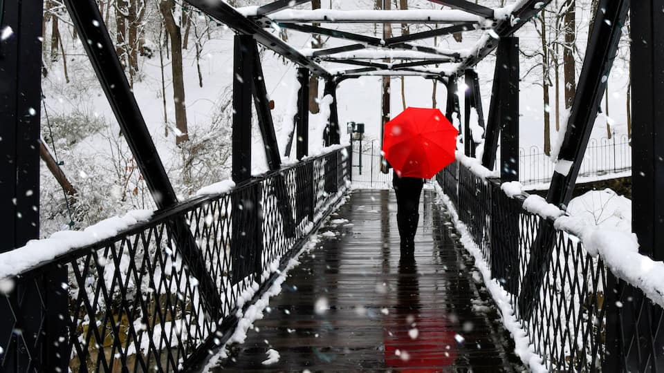 A snow-covered bridge with metal railings and a red umbrella.
