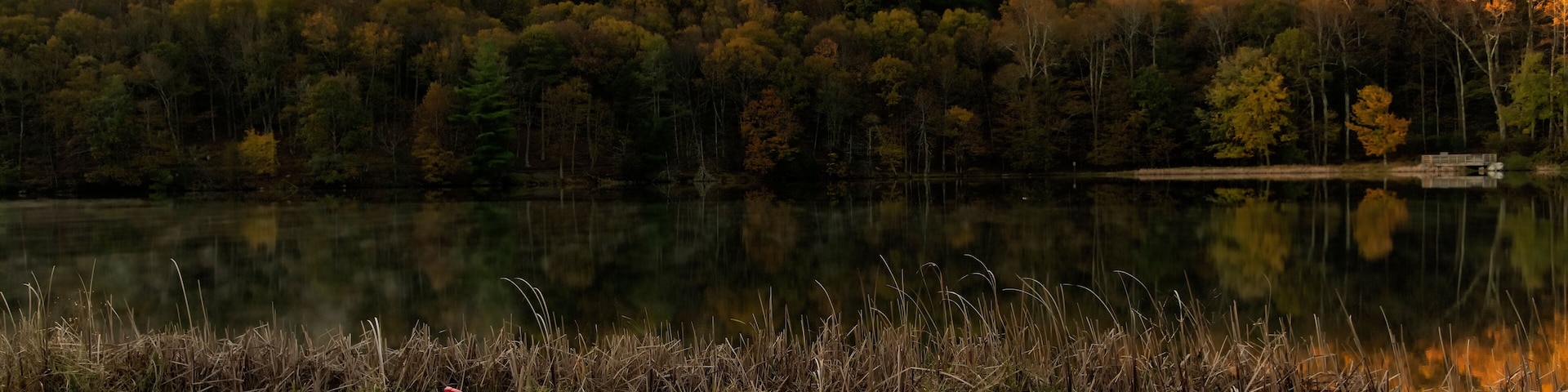 Um lago com cadeiras Adirondack vermelhas e uma colina arborizada ao fundo.
