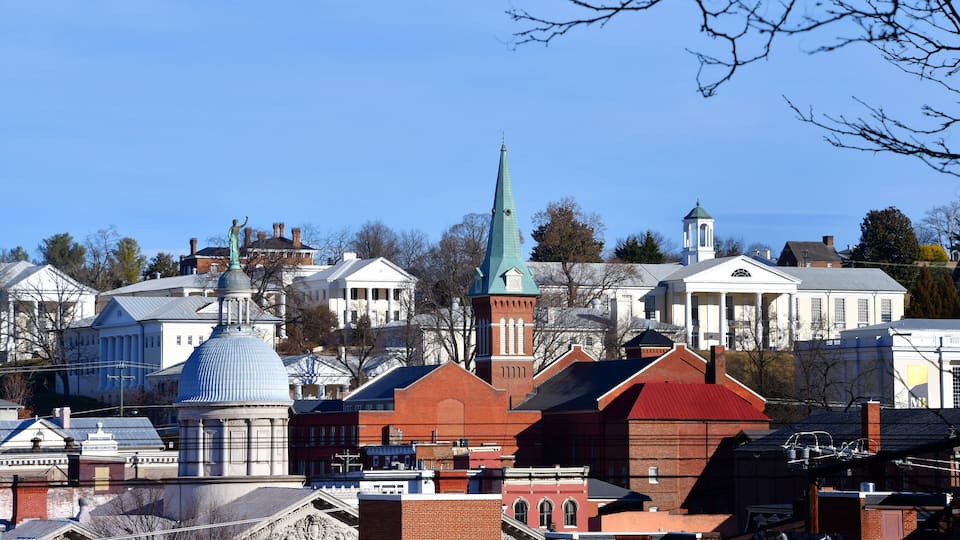 A cityscape with prominent buildings, including a church with a green spire and a dome, and a white building with columns.