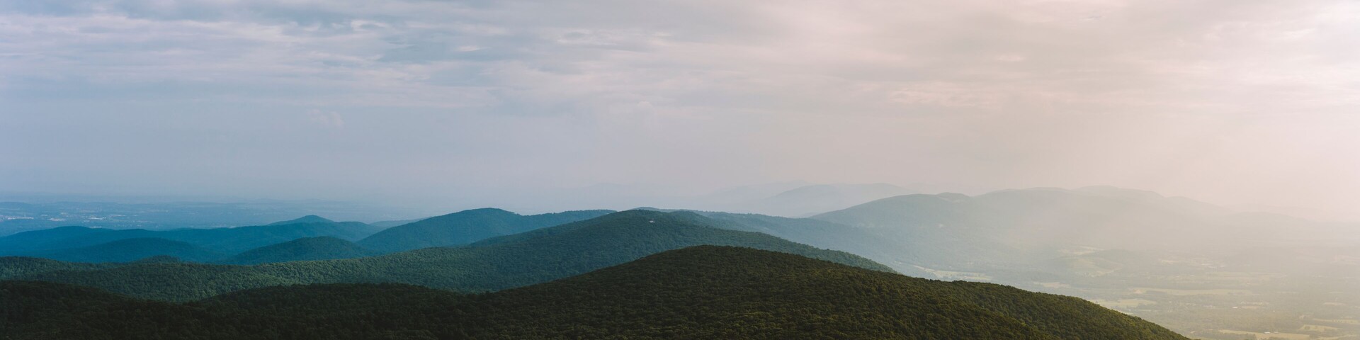 A panoramic view along the Blue Ridge Mountain range on a summer afternoon as the sun pierces through the clouds in Afton, VA.