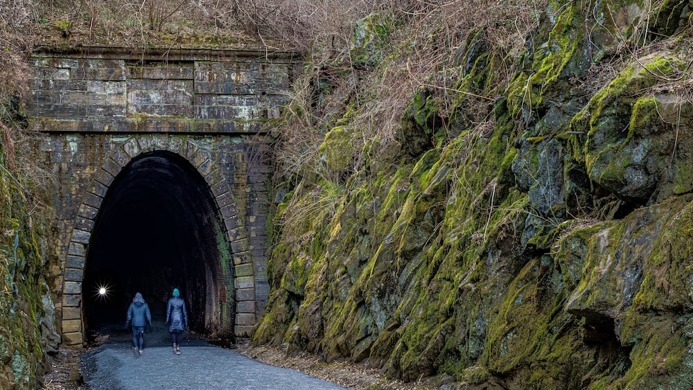 Un tunnel en pierre dont les murs sont recouverts de mousse, et une colline rocheuse.