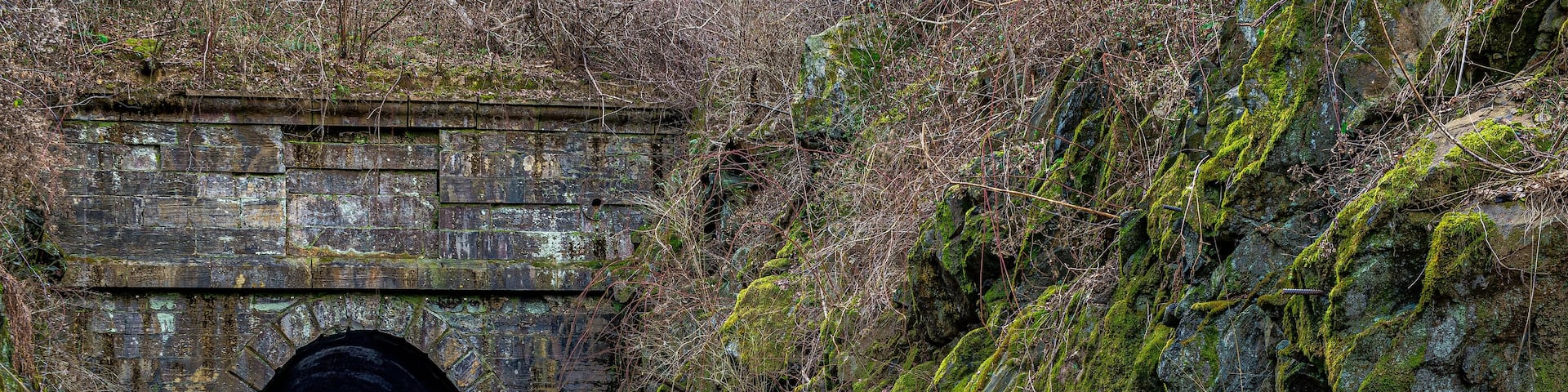 A stone tunnel with moss-covered walls and a rocky hillside.