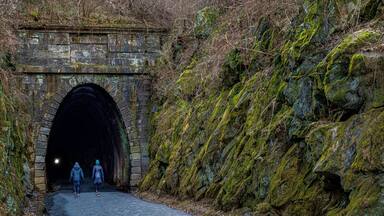 Un túnel de piedra con paredes cubiertas de musgo y una ladera rocosa.