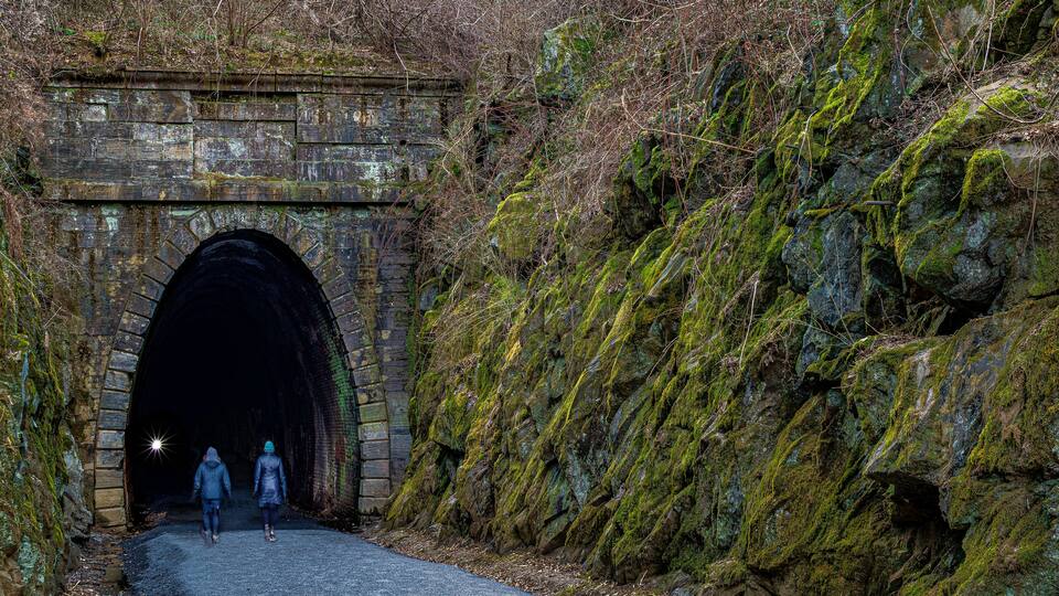 A stone tunnel with moss-covered walls and a rocky hillside.