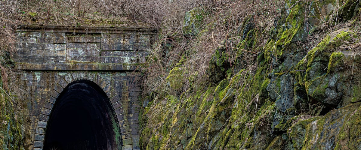 A stone tunnel with moss-covered walls and a rocky hillside.