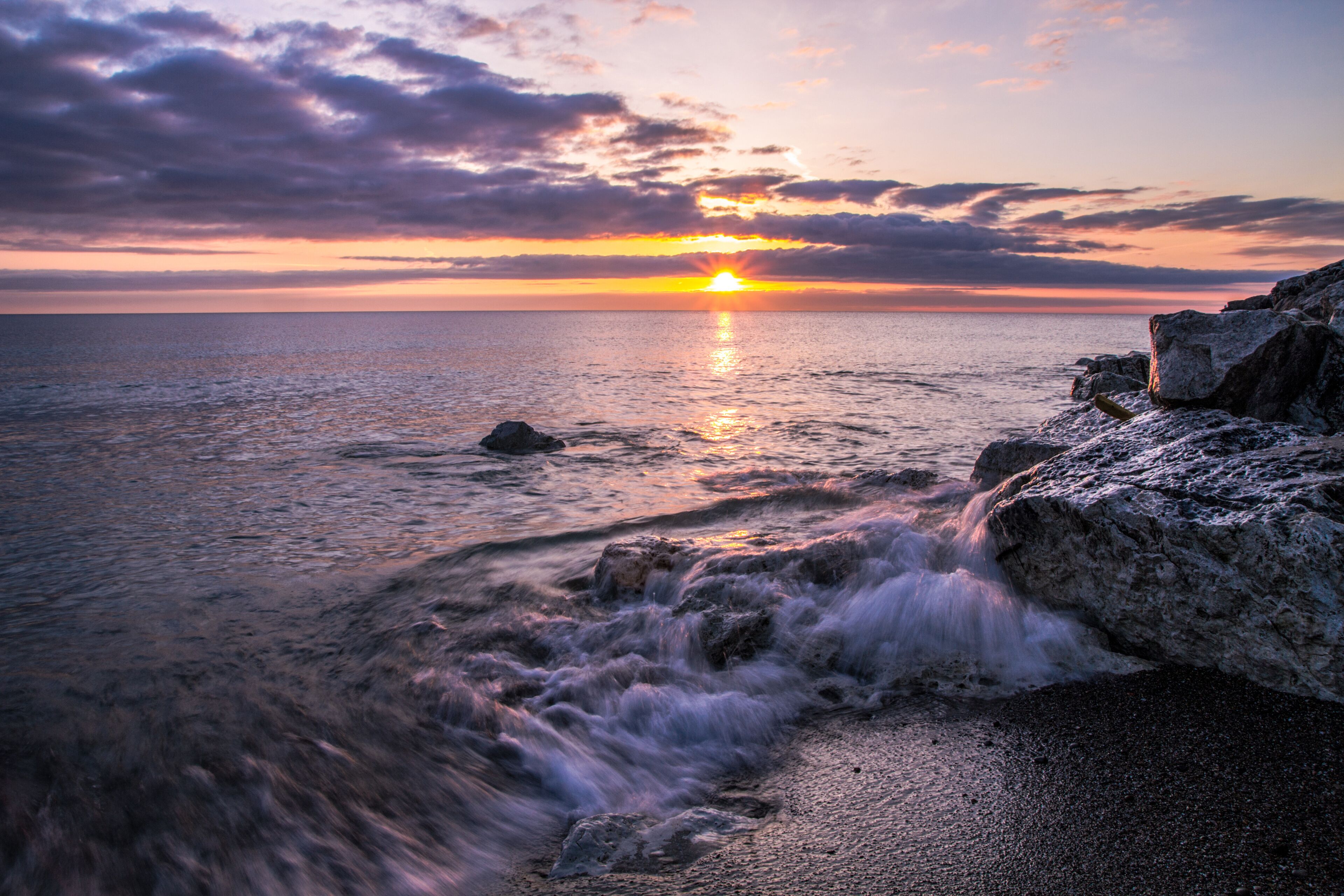 Un atardecer sobre un mar tranquilo, con olas rompiendo sobre una costa rocosa.