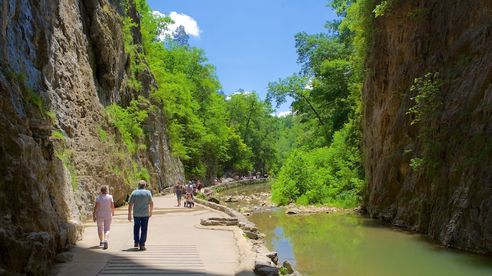 A pathway along a river surrounded by rocky cliffs and lush greenery.