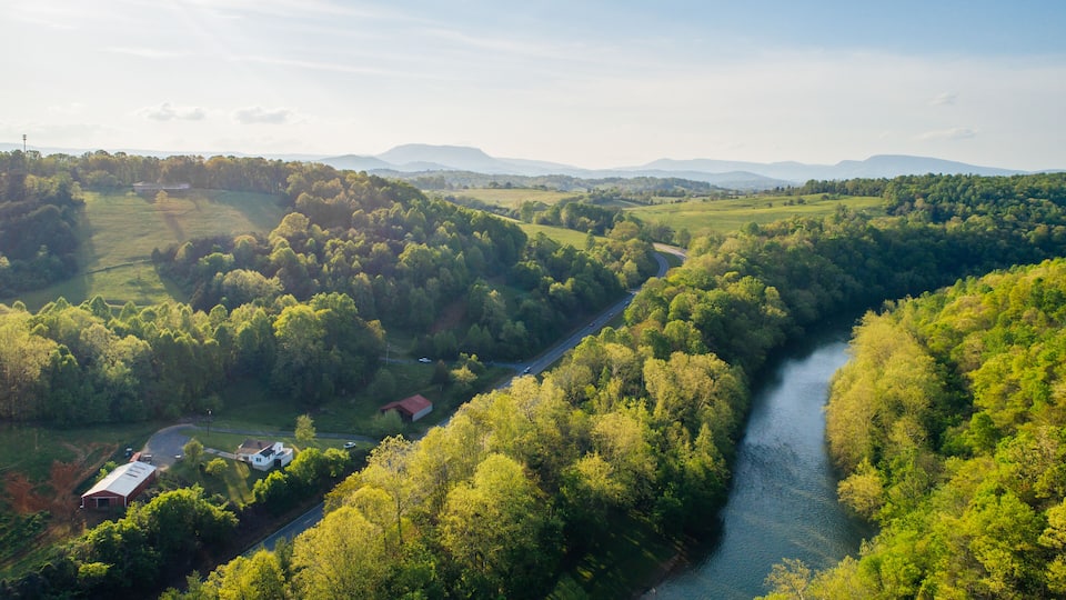 A river winding through a lush valley with dense forests and rolling hills in the background.