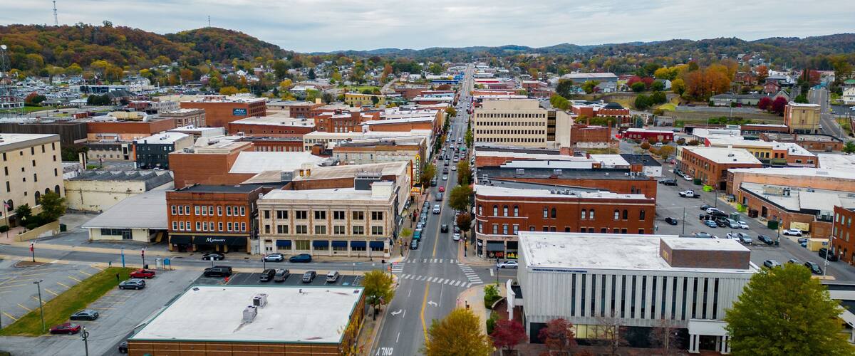 A town with a main street lined with buildings, a parking lot, and autumn-colored trees.