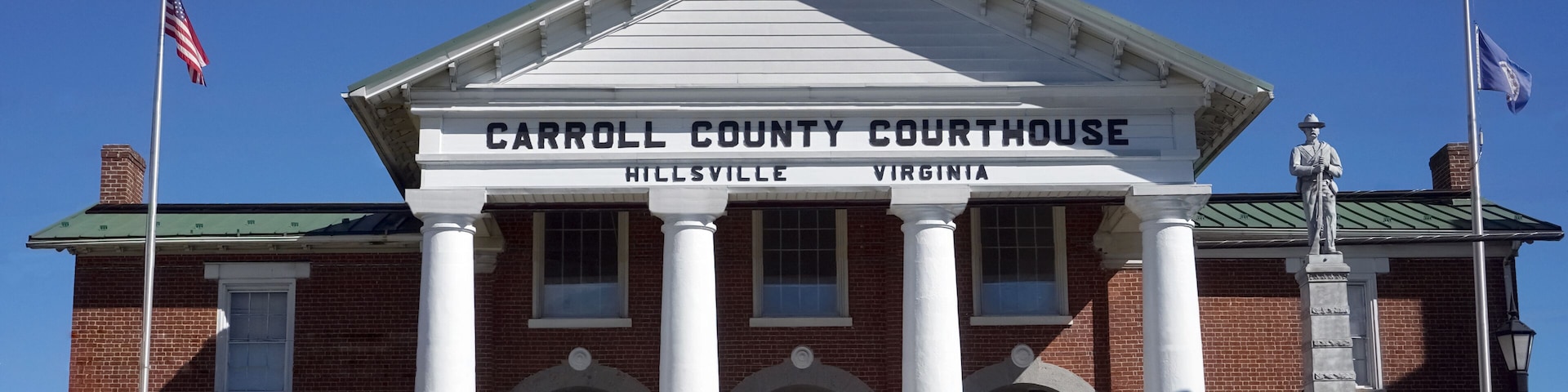 Palacio de la Corte del Condado de Carroll en Hillsville, Virginia, con una entrada destacada, columnas blancas y una estatua.