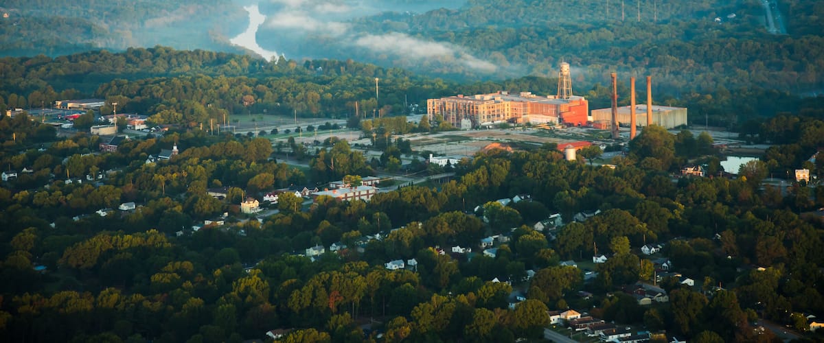 A large industrial complex surrounded by dense forests and a river.
