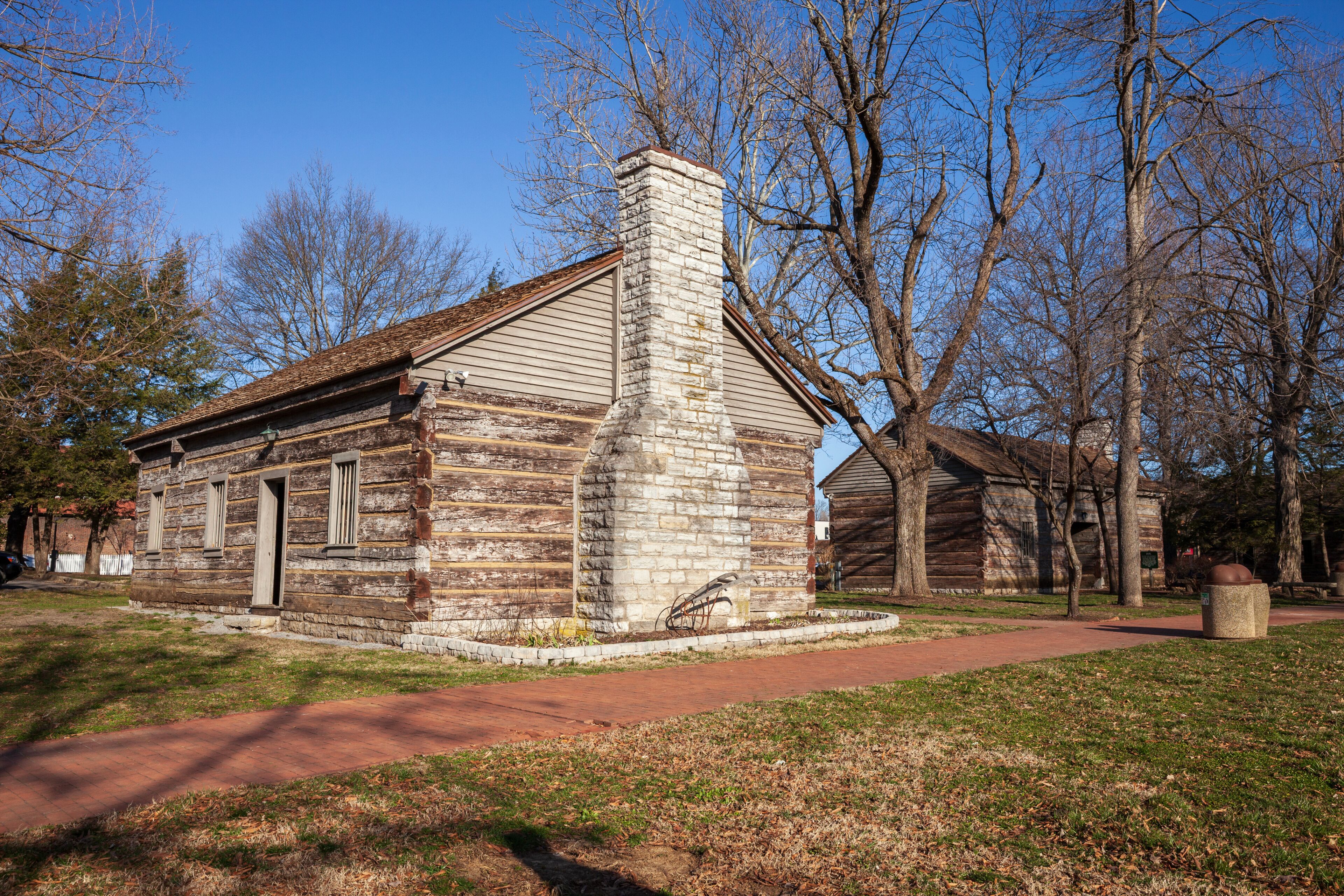 A historic log cabin with a stone chimney, surrounded by trees and a clear sky.