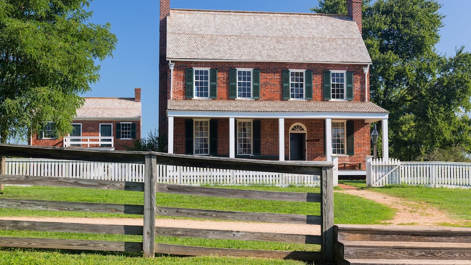 A historic brick house with a white picket fence and green shutters.