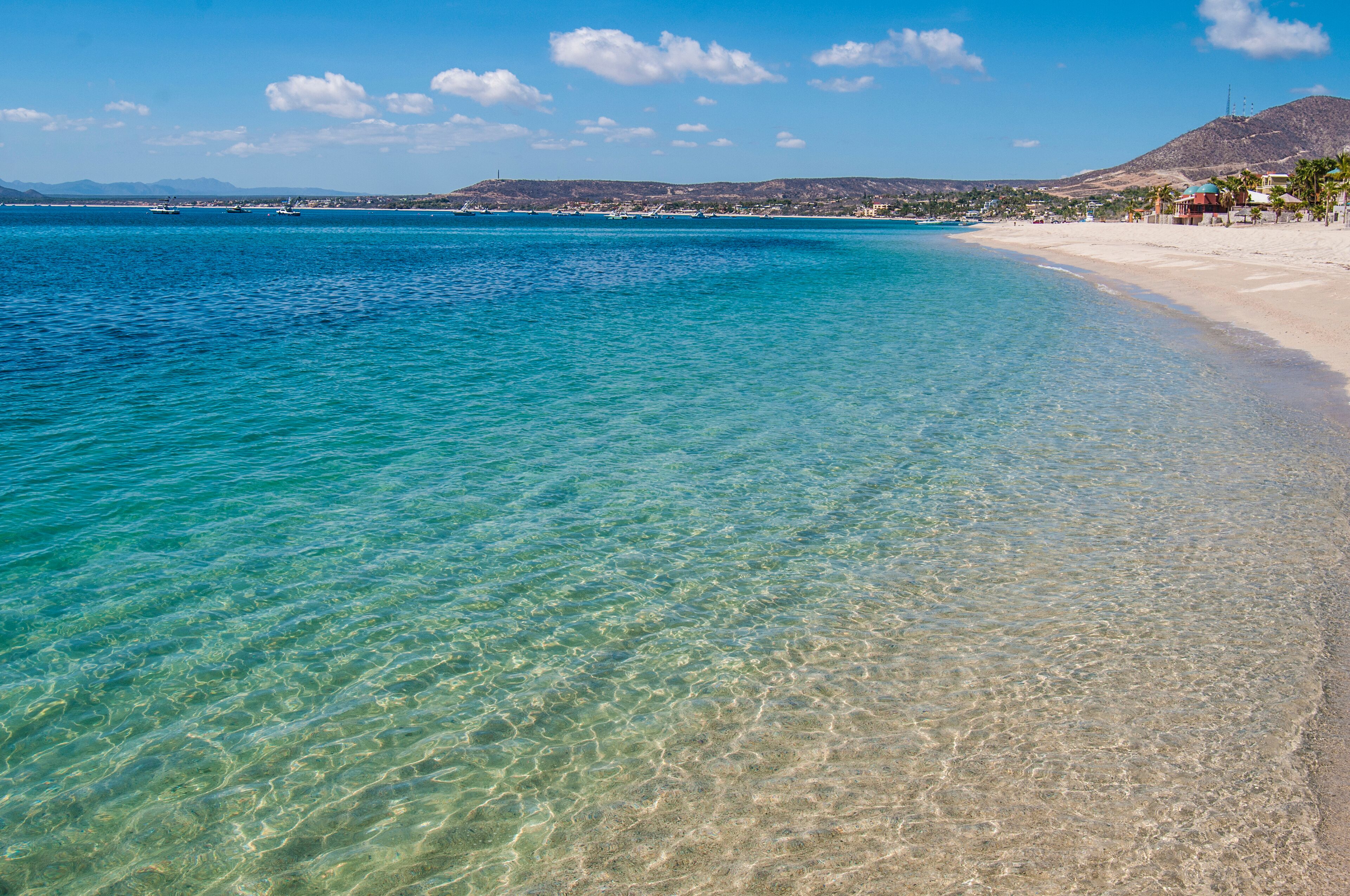 A clear turquoise sea, a sandy beach, and a distant mountain range.