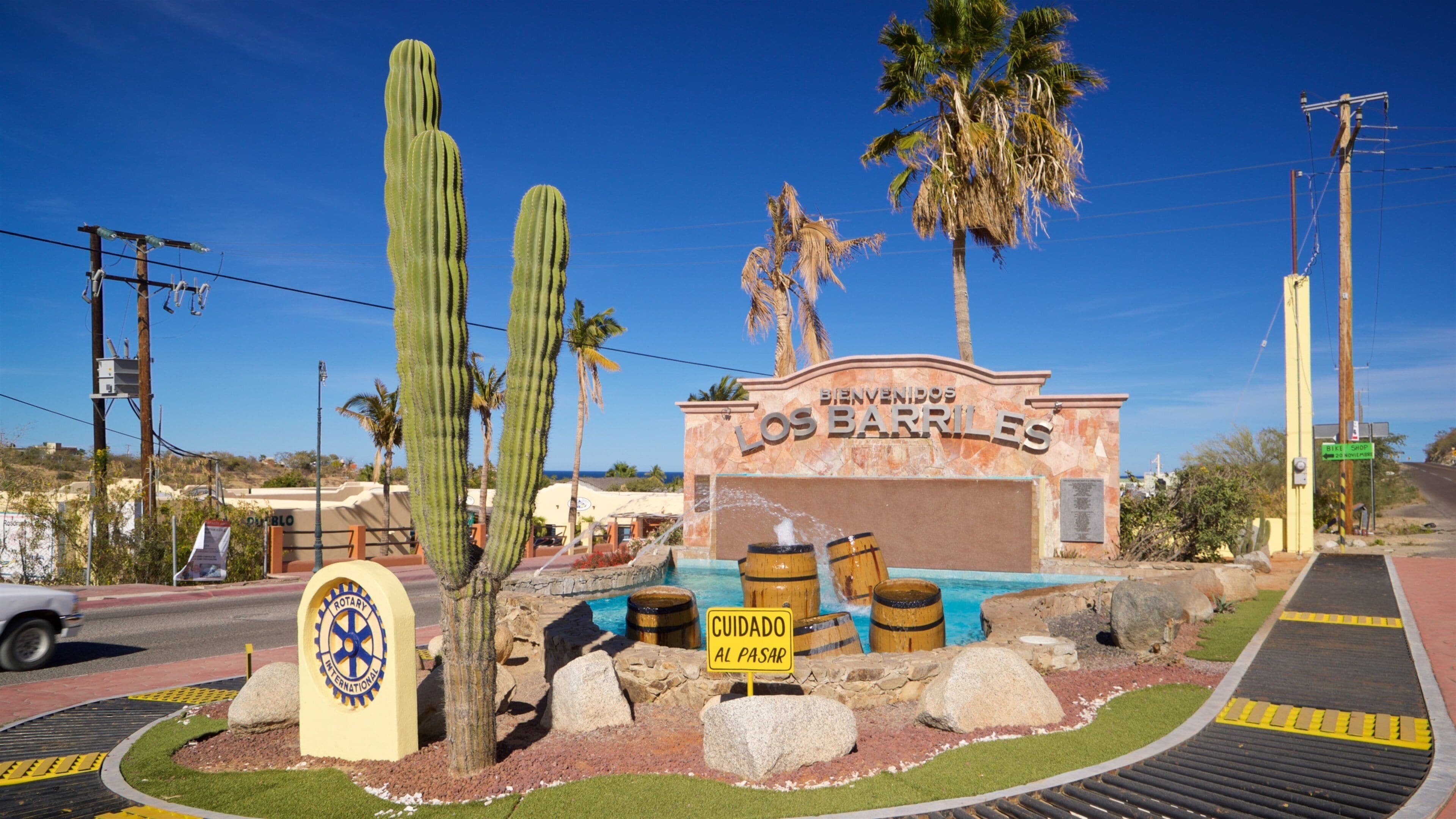 A sign for 'Bienvenidos Los Barriles' with a pool, cacti, and palm trees.