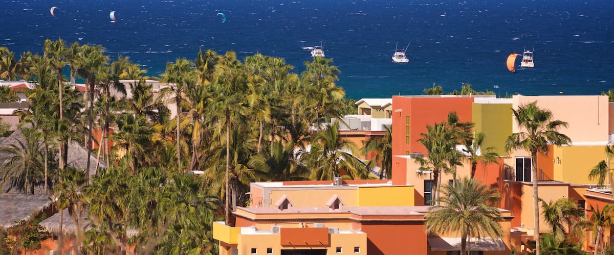 Un pueblo costero con palmeras, edificios coloridos y vistas al océano donde se practica kitesurf.