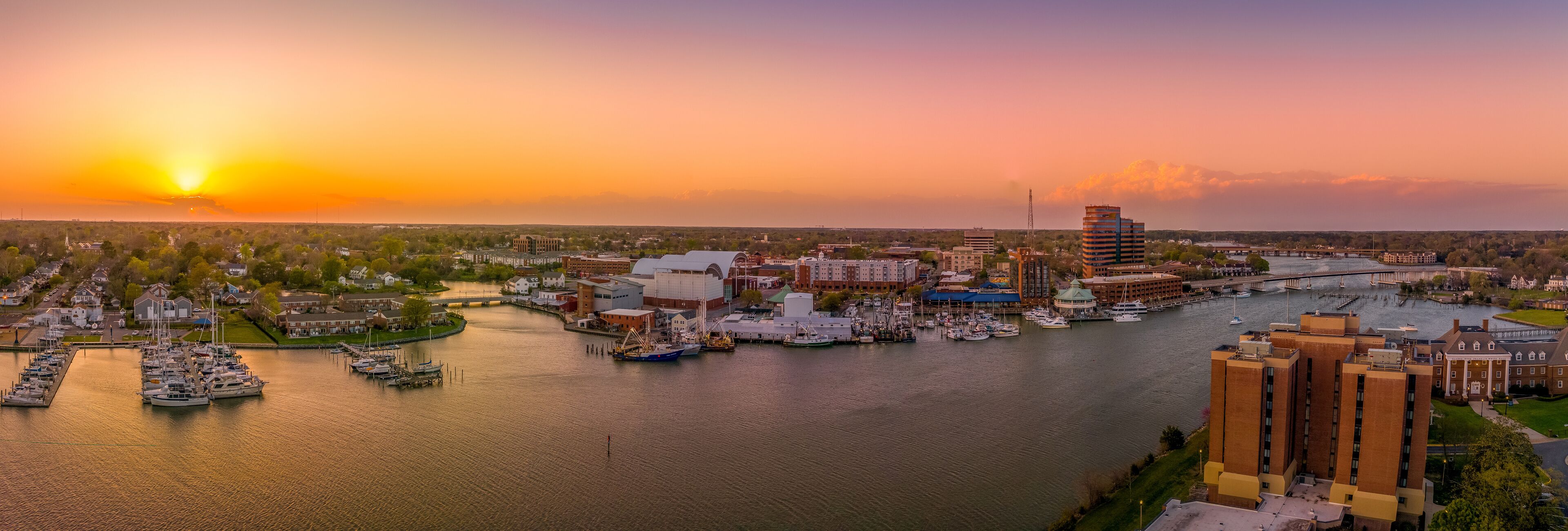 A marina with boats docked, a river, and buildings along the riverbank.