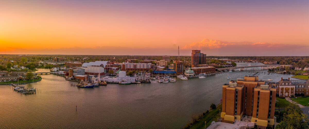 A marina with boats docked, a river, and buildings along the riverbank.