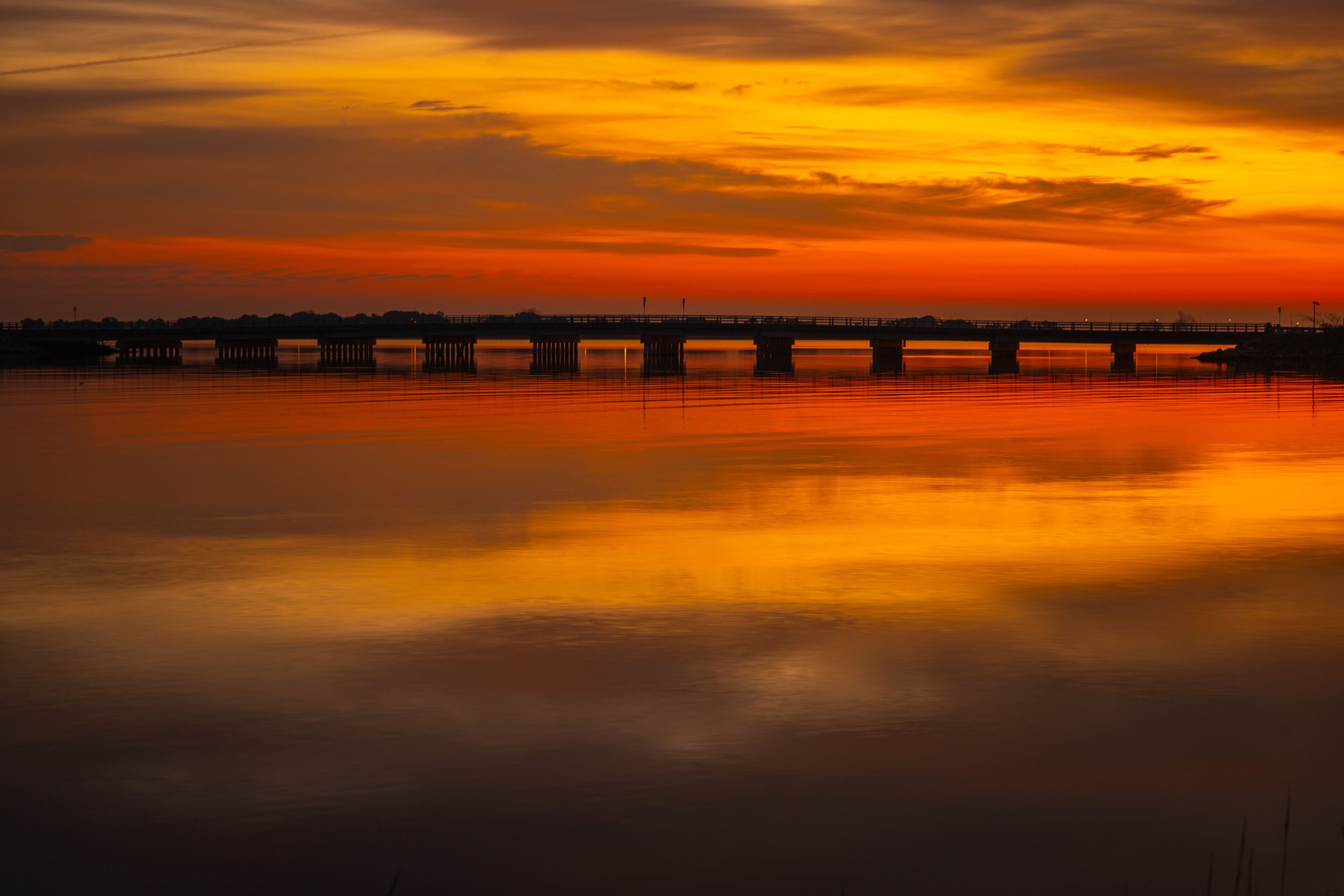 A sunset over a calm river with a bridge in the distance.