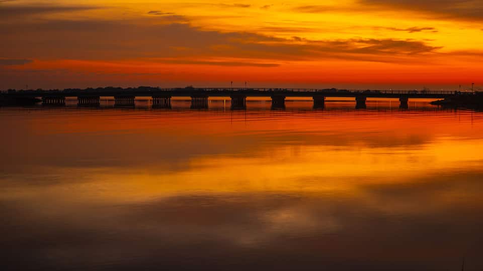 A sunset over a calm river with a bridge in the distance.