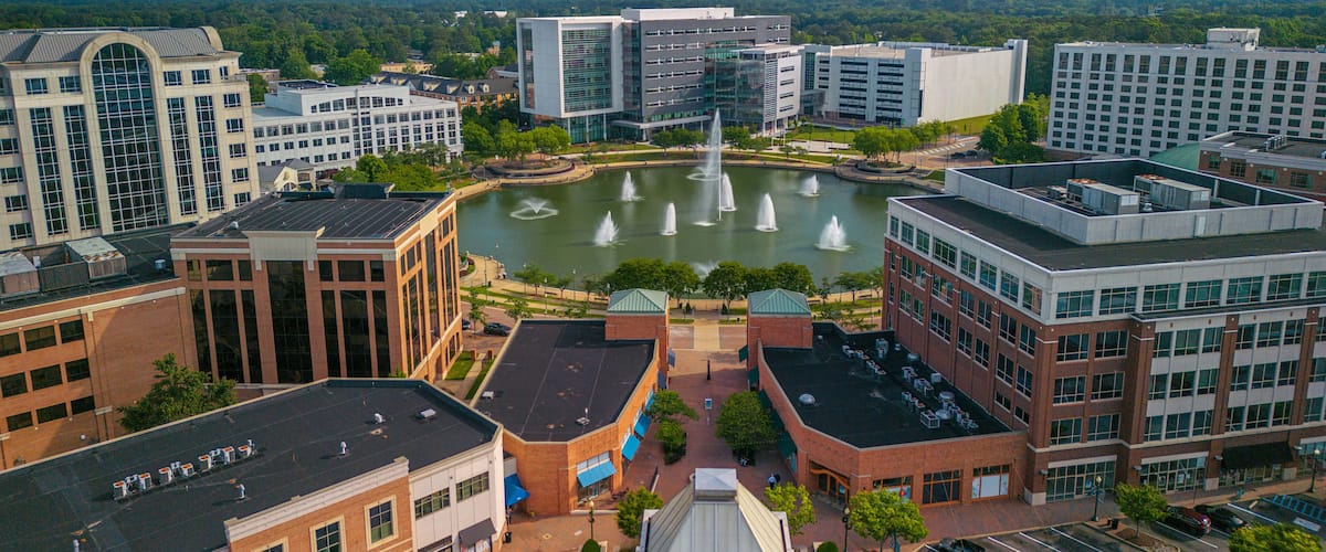 A cityscape with modern buildings, a central fountain, and a surrounding park.
