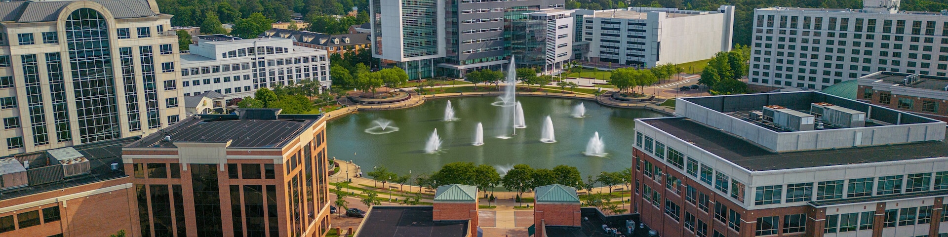 A cityscape with modern buildings, a central fountain, and a surrounding park.