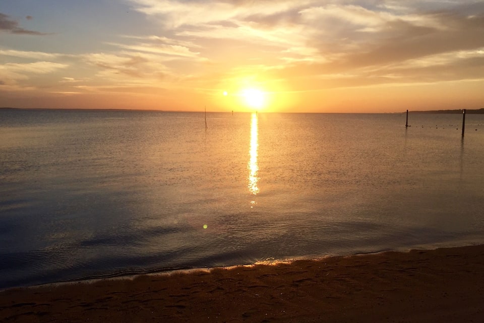 Un atardecer sobre un mar tranquilo con una playa en primer plano.