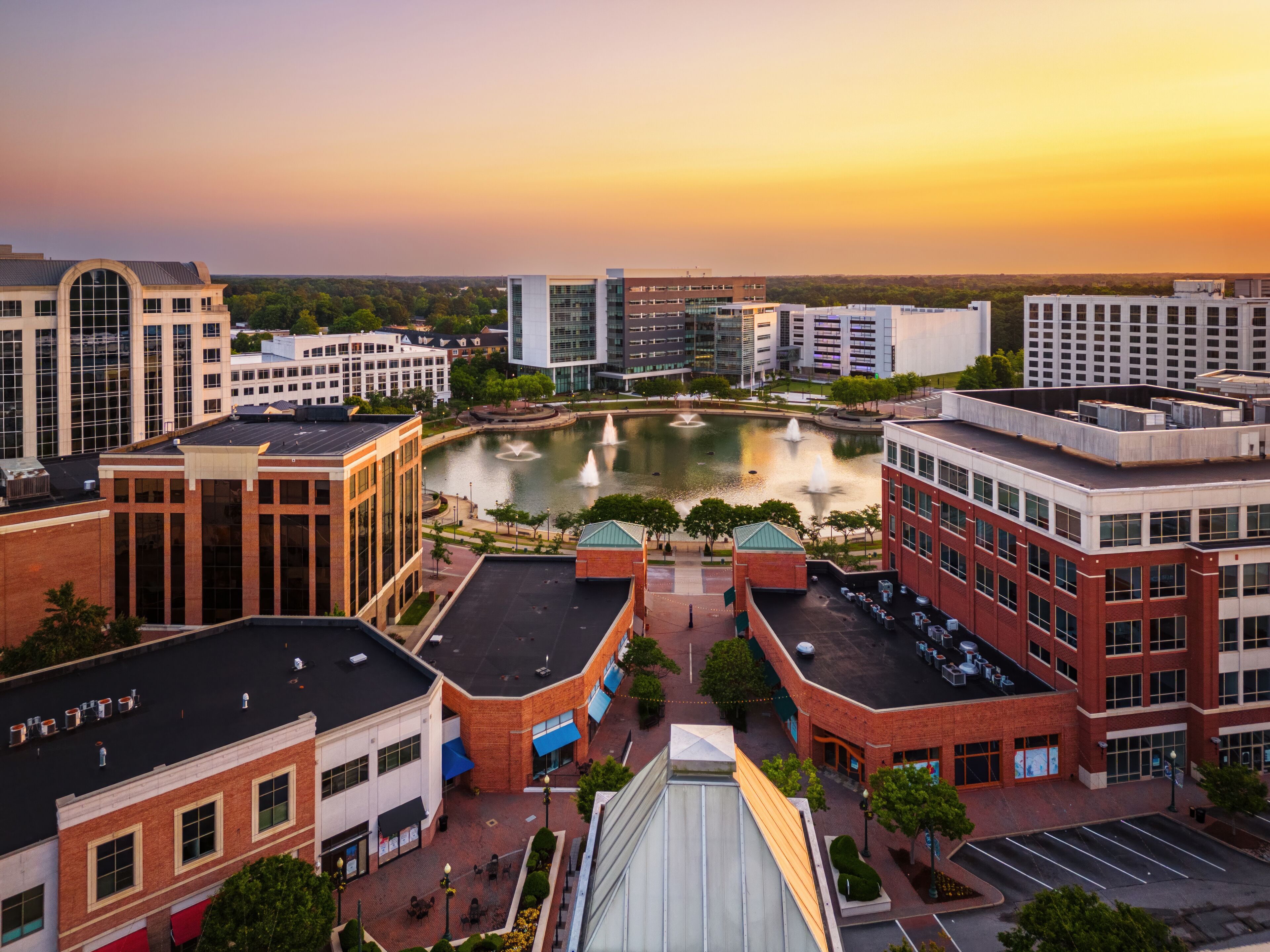 A cityscape with a central pond, surrounding buildings, and a sunset sky.