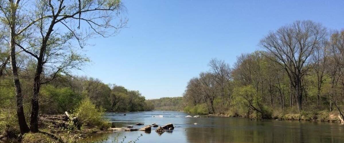 A calm river with clear water, surrounded by trees and rocks.