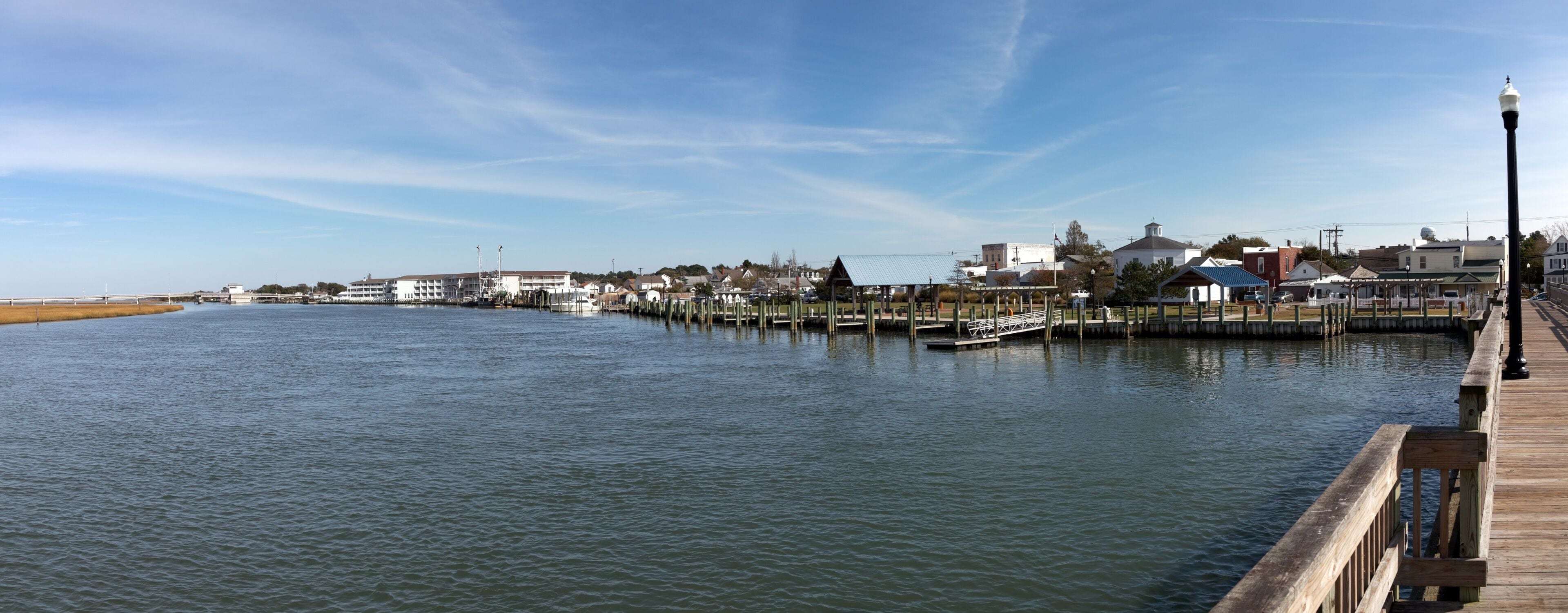 A waterfront with a wooden pier, buildings, and a clear sky.