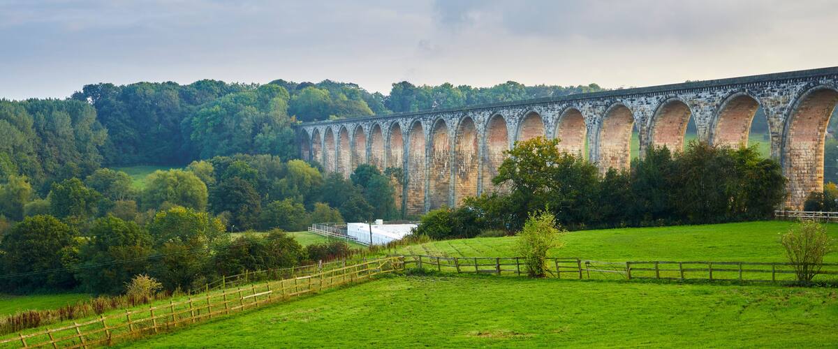 A stone viaduct over a lush green valley with a wooden fence in the foreground.
