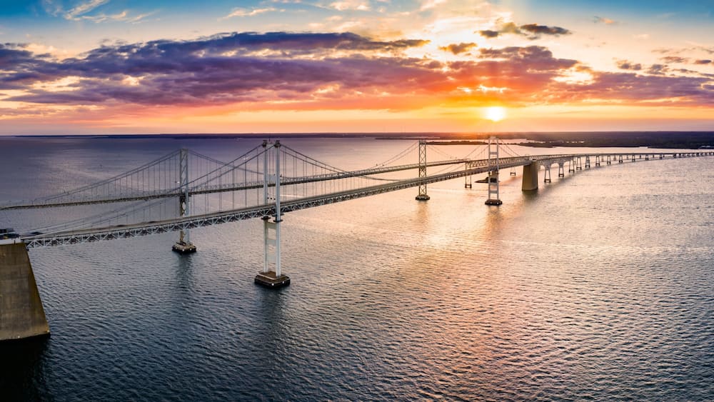 A suspension bridge over a body of water with a sunset in the background.