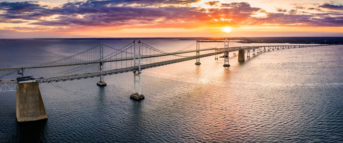 A suspension bridge over a body of water with a sunset in the background.