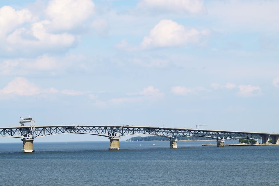 A large steel bridge spanning a wide river with a clear sky and distant landmass.