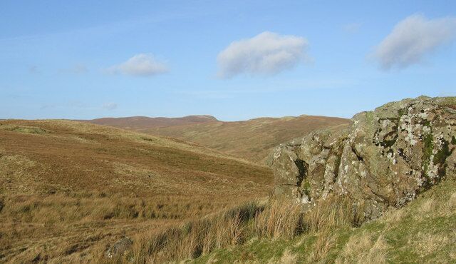 Rolling hills, a rocky outcrop, and distant hills under a clear sky.