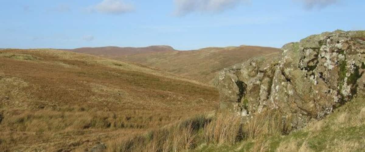 Rolling hills, a rocky outcrop, and distant hills under a clear sky.