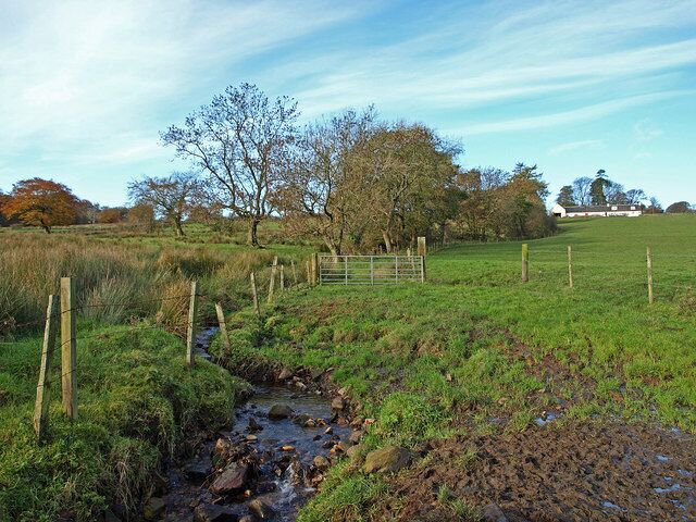 A rural landscape with a stream, grassy fields, a wooden fence, and trees.