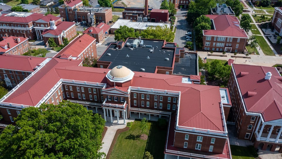 A large red-brick building with a central dome, surrounded by smaller buildings and green spaces.