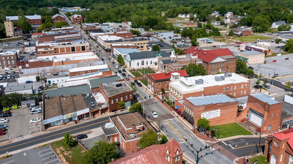 An aerial view of a small town with a mix of historic and modern buildings, a main street, and surrounding greenery.