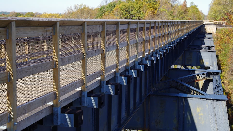 A wooden pedestrian bridge with metal railings, spanning over a railway track.