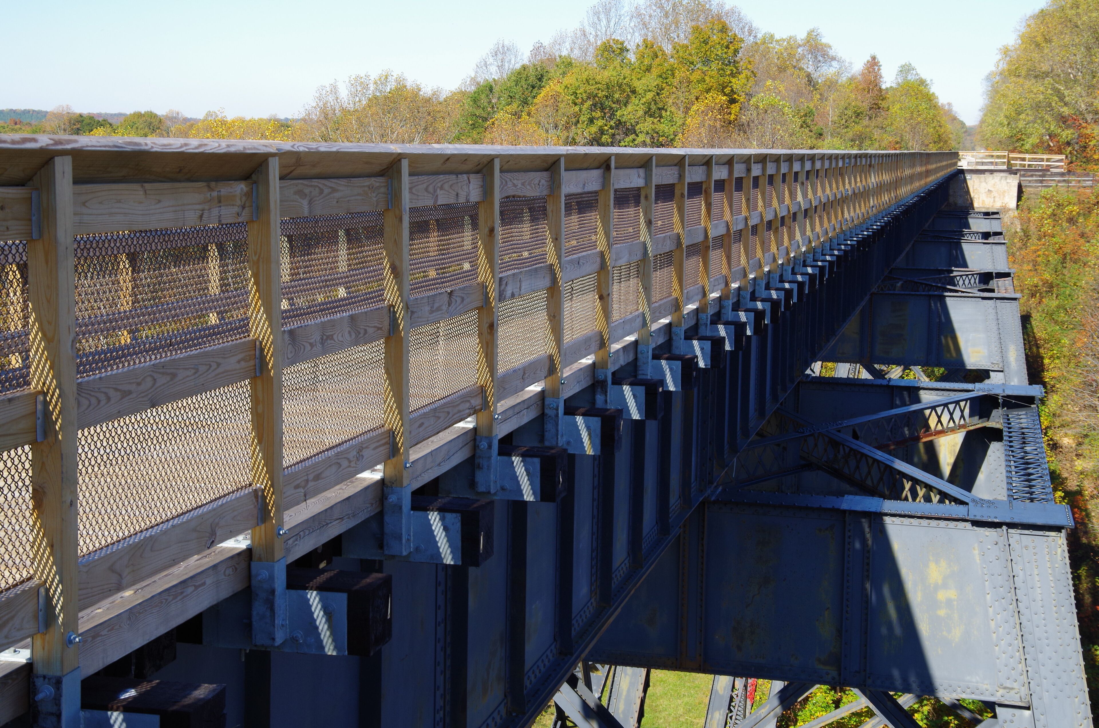 A wooden pedestrian bridge with metal railings, spanning over a railway track.
