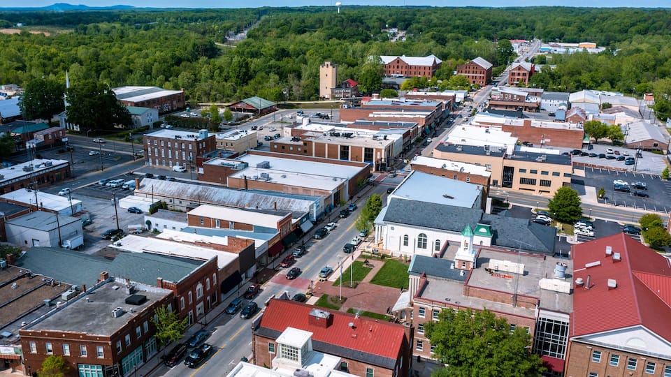 A town with a main street lined with historic buildings, a church, and a large green park in the background.