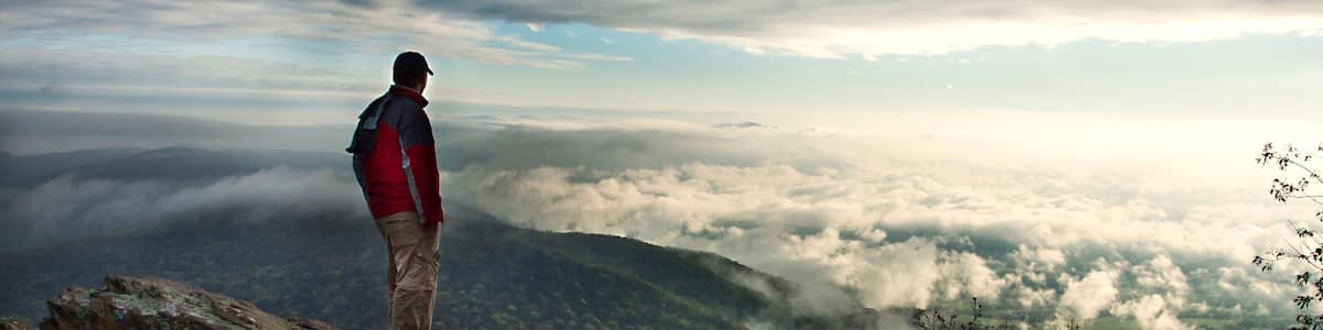 Une personne se tient sur un promontoire rocheux, surplombant une vallée de nuages.