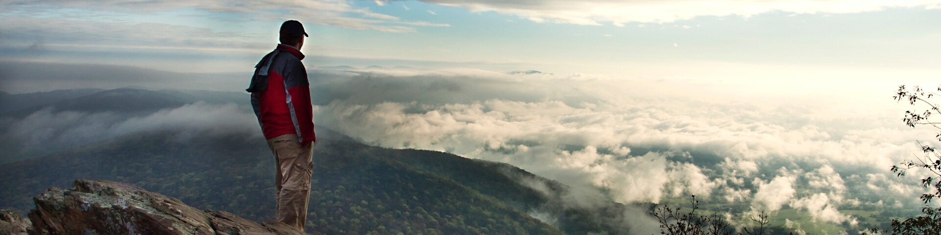 A person standing on a rocky outcrop overlooking a valley of clouds.