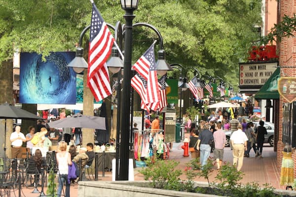 A bustling outdoor market with American flags, street lamps, and various shops.