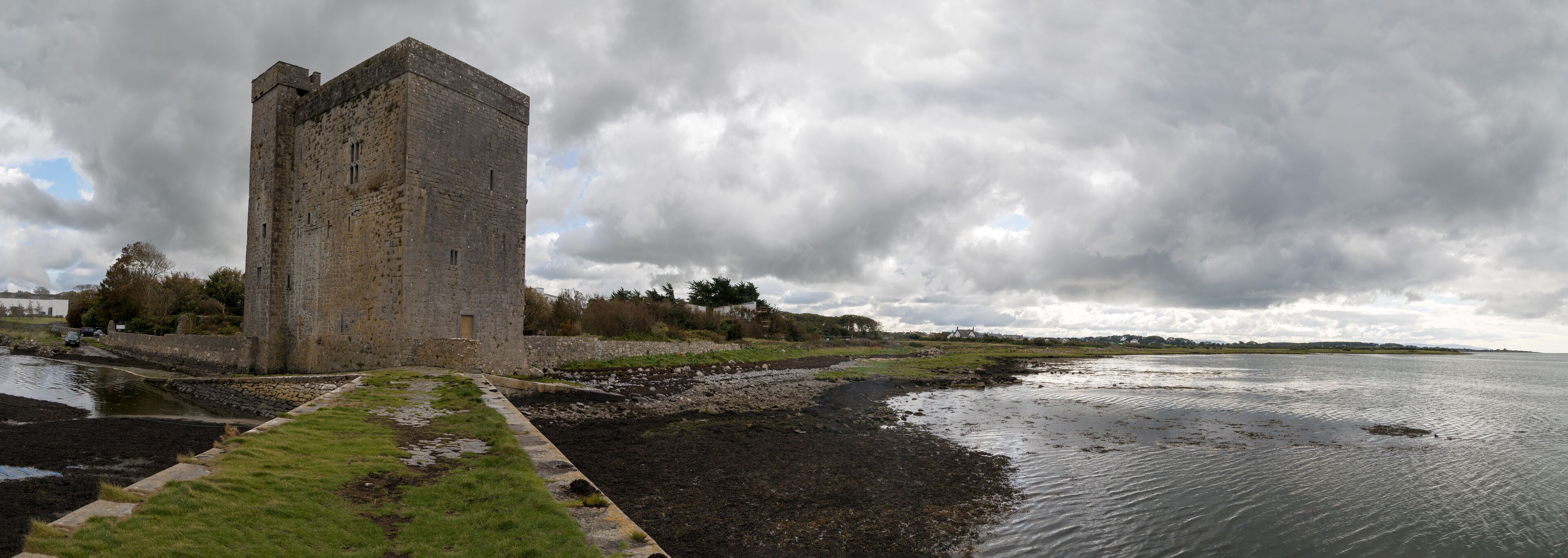 A historic stone tower by a calm river with a cloudy sky.