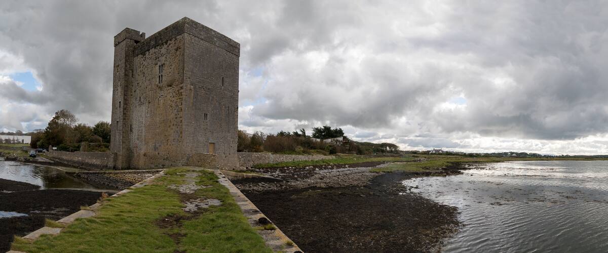 A historic stone tower by a calm river with a cloudy sky.