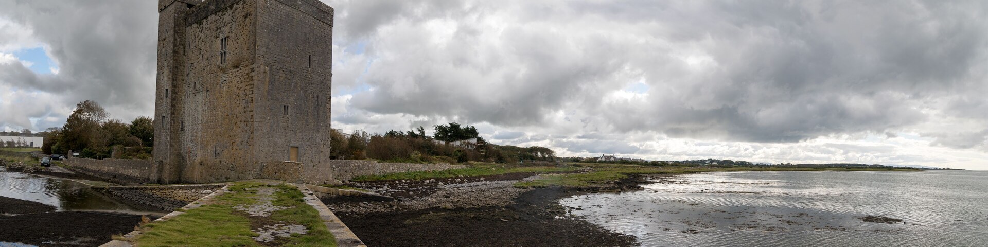 A historic stone tower by a calm river with a cloudy sky.