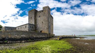A historic stone tower by a rocky shoreline with a body of water and a cloudy sky.