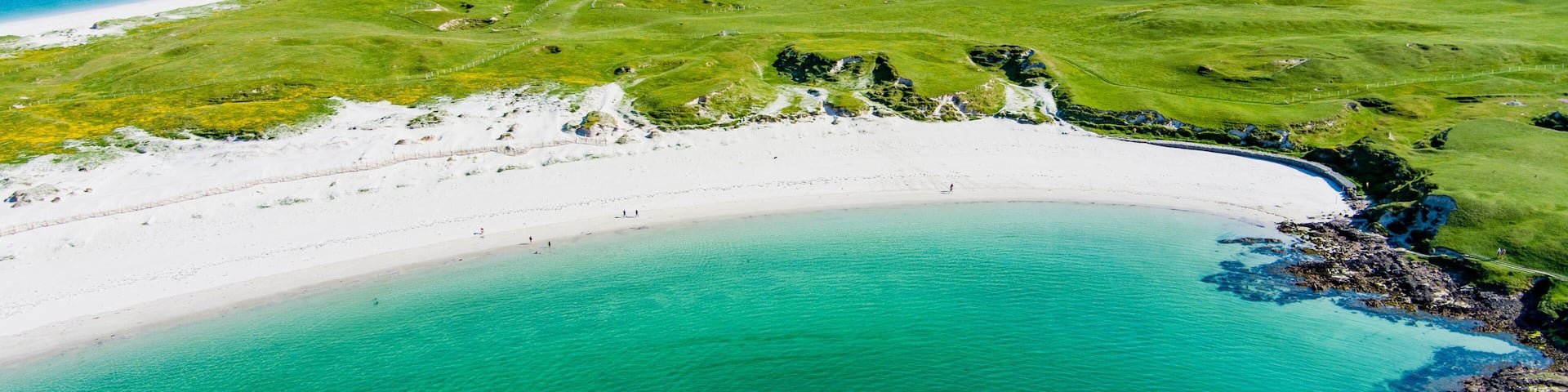 A coastal landscape with a sandy beach, a grassy area, and a clear blue sea.